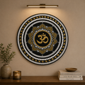 Decorative wall art with Om symbol on a beige wall above a wooden shelf.